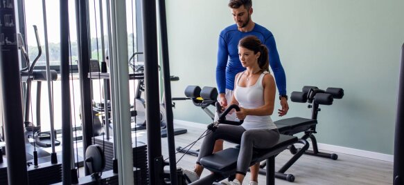 Osobni trener pomaže ženi tijekom vježbanja na fitness spravi u teretani